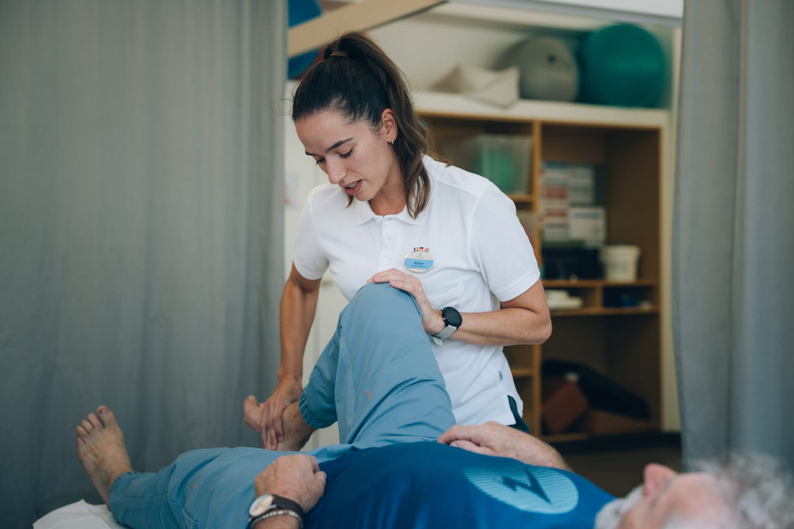 Eine Therapeutin bewegt das gebeugte Knie eines Patienten, der auf der Behandlungsliege liegt